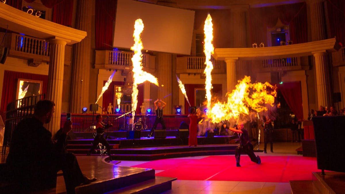 Fireshow with big fire effects, flamethrower and fire artists in a columned hall.