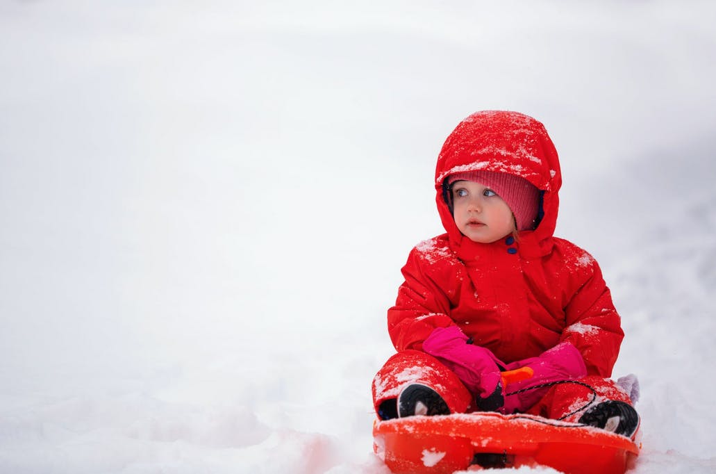 a baby wearing a red snowsuit on a sled