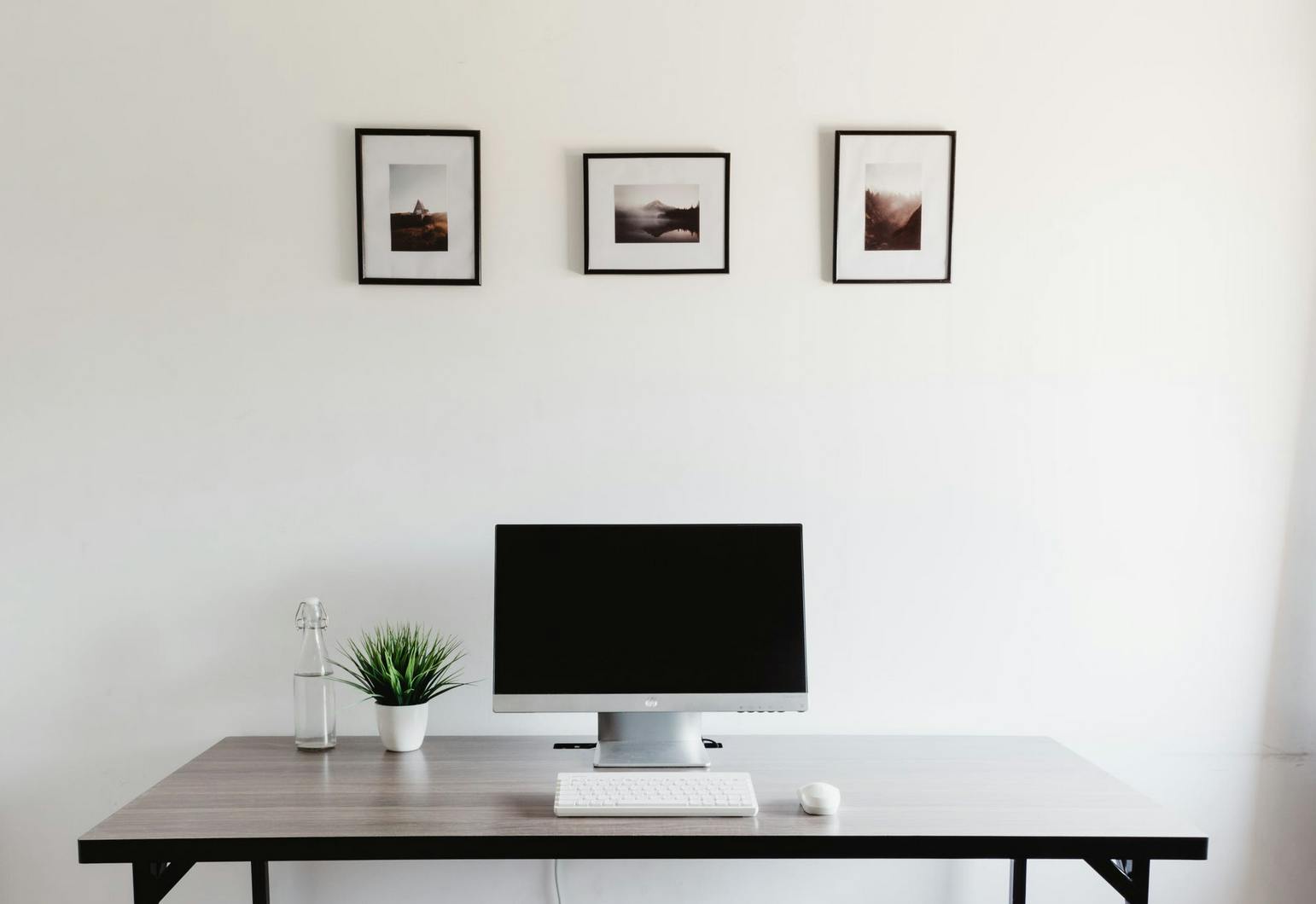 a minimalist office set up with computer and pictures on wall