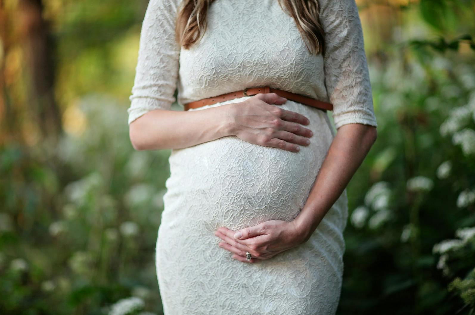 woman in white dress holding her pregnant stomach