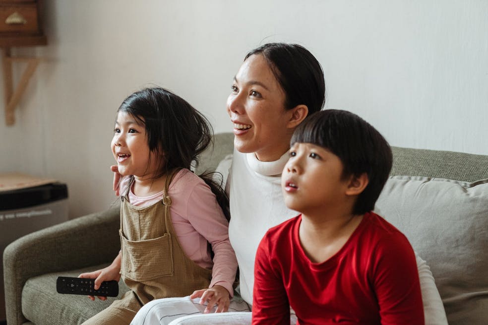 mom and two children watching tv on the couch