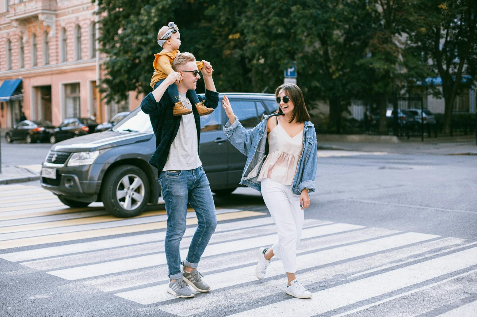 mom and dad walking on city crosswalk with baby on shoulders