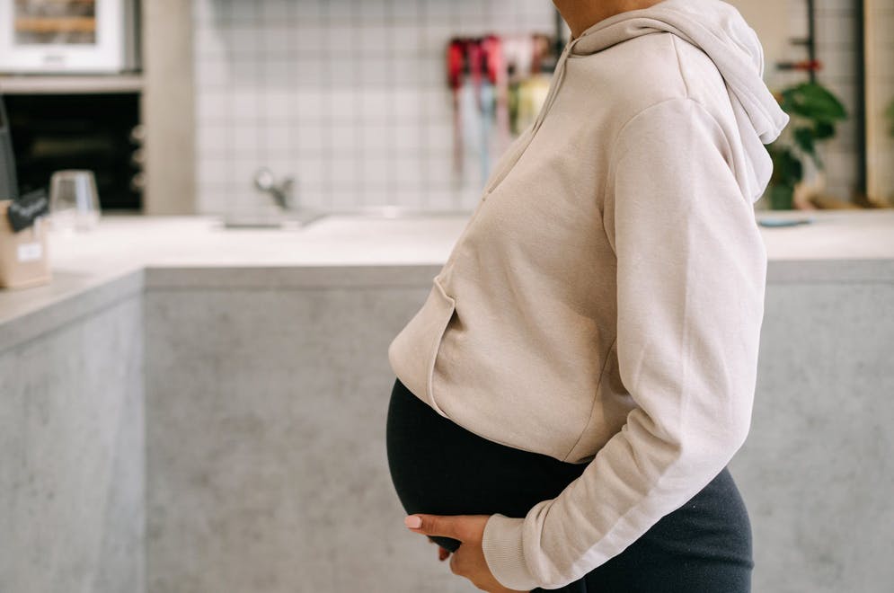 woman in yoga pants and sweatshirt holding her pregnant stomach