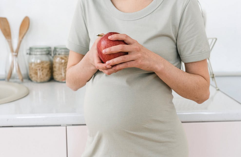 pregnant woman holding a red apple in the kitchen
