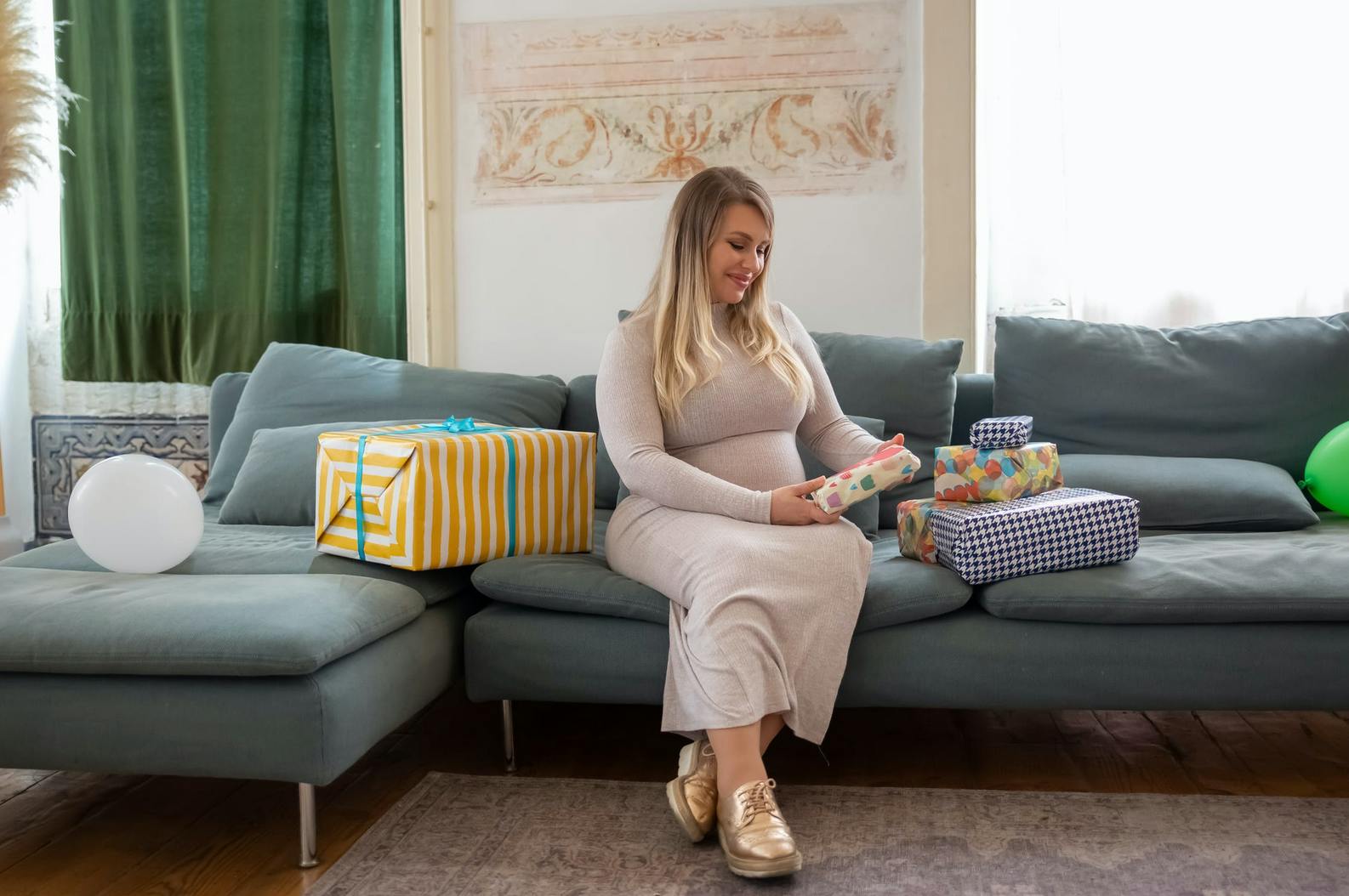 pregnant woman on green couch opening gifts