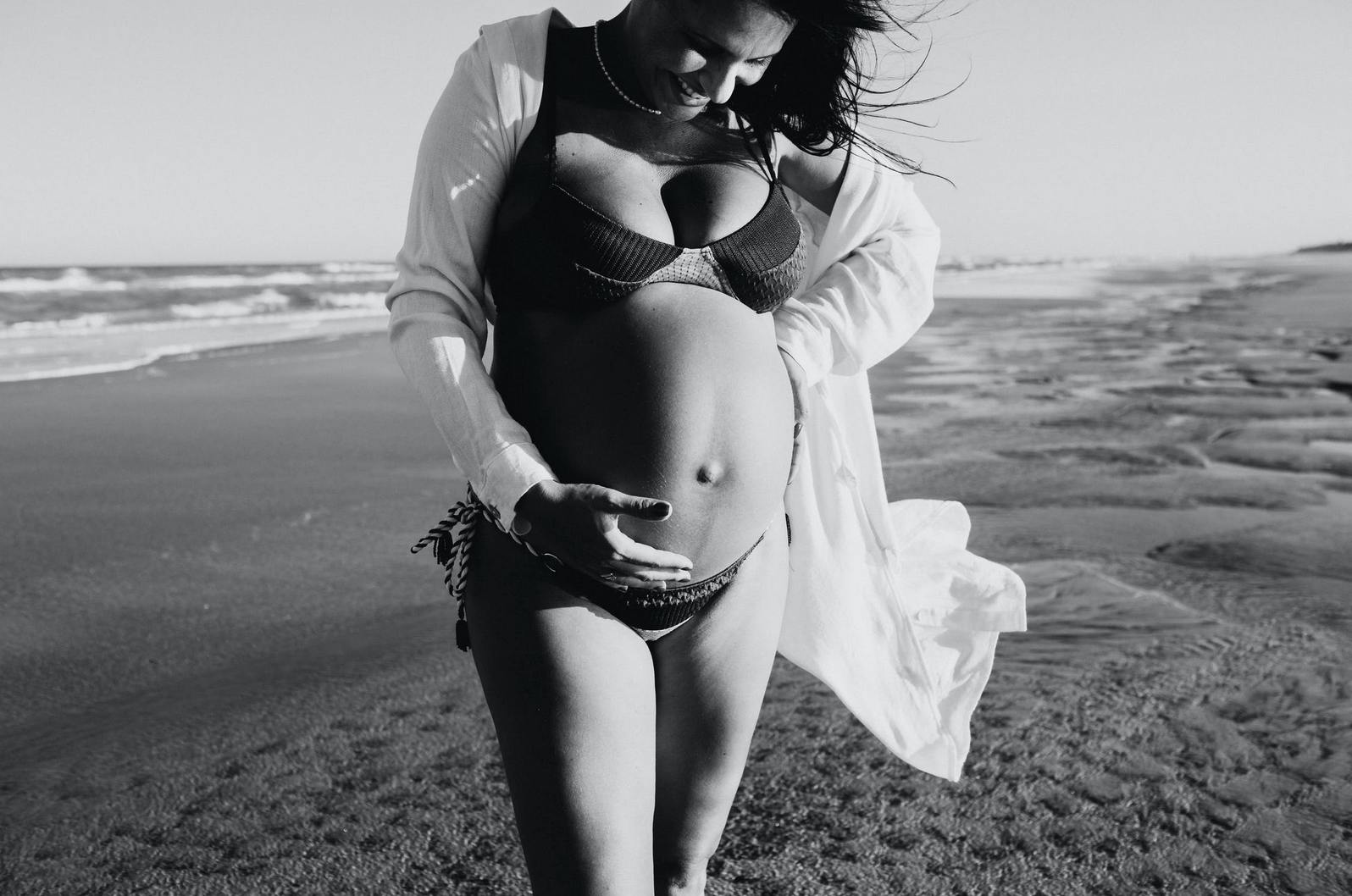 a mom in a bikini holding her pregnant stomach on the beach