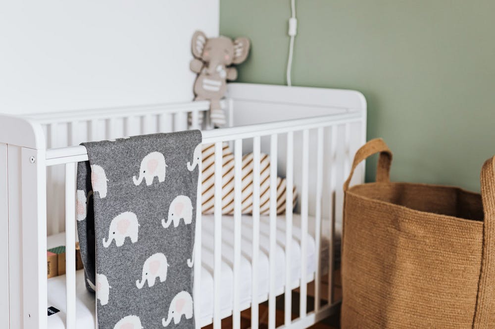 baby crib with gray blanket and stuffed elephant