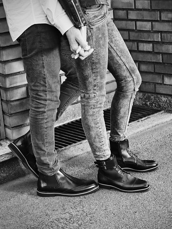 A young couple wearing black leather shoes in front of a brick wall.