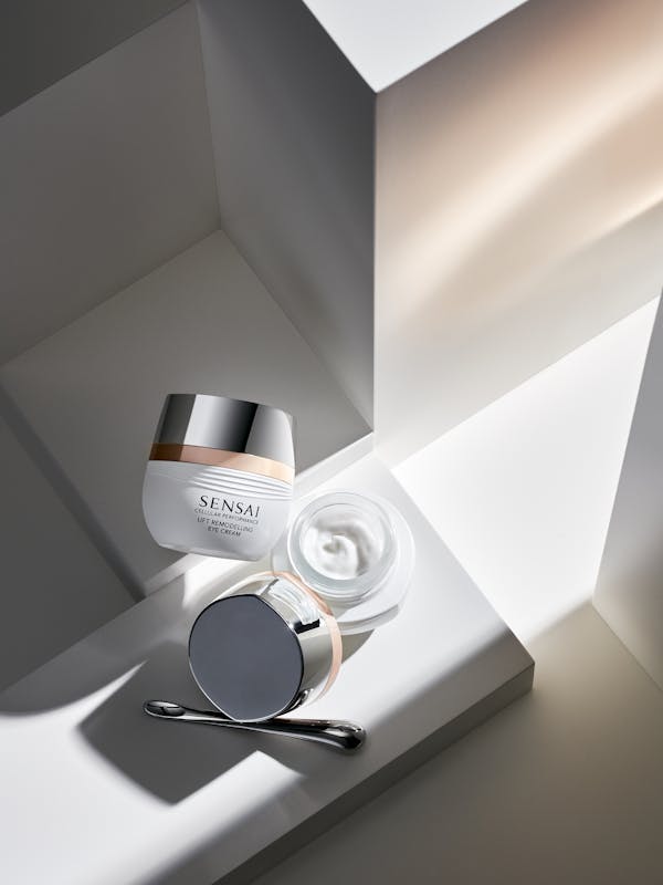 A white box containing beauty cream on white pedestals, with golden light shining in from the right-hand side.