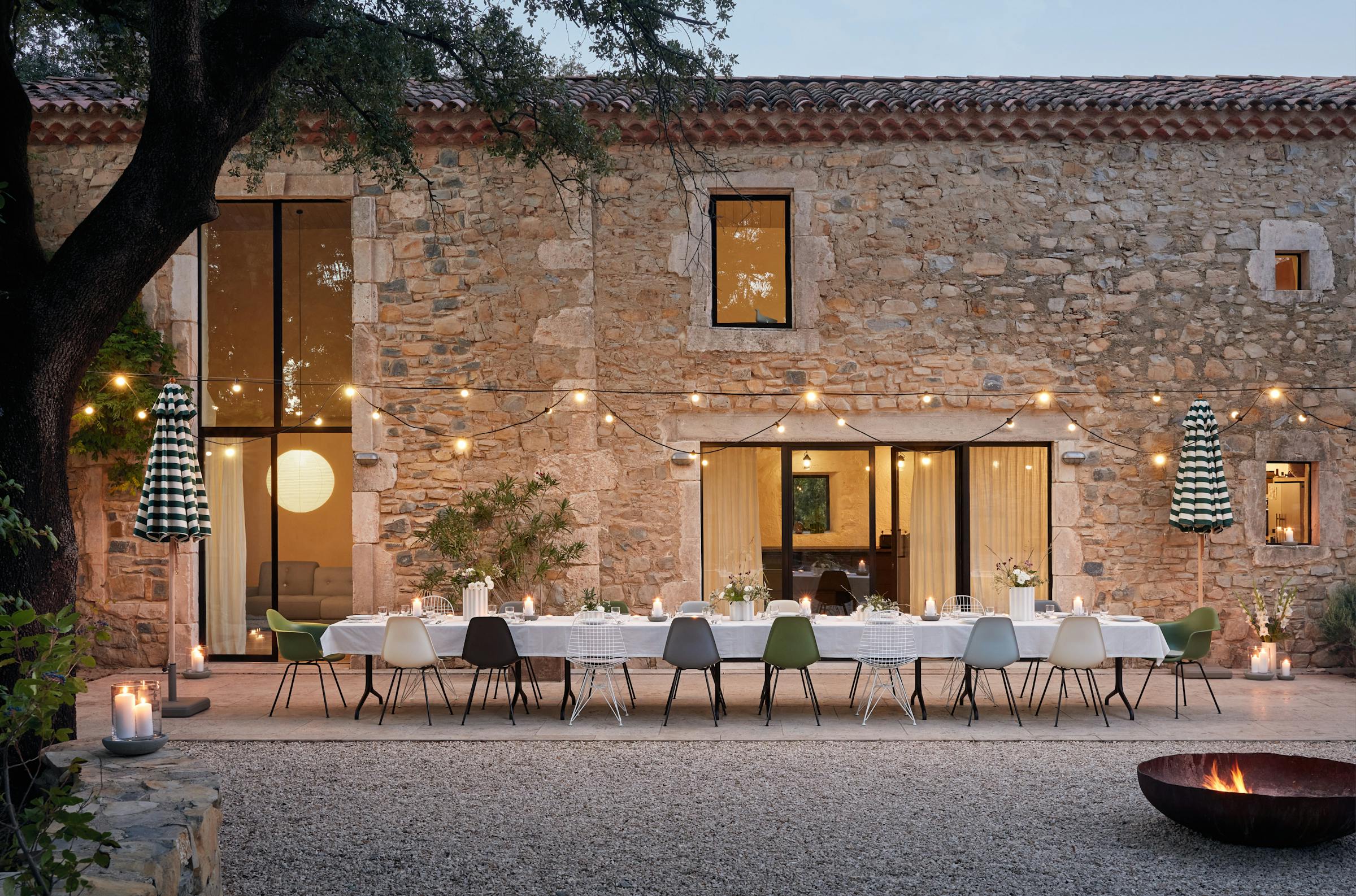 Courtyard with a long white-covered dining table and many different chairs at dusk