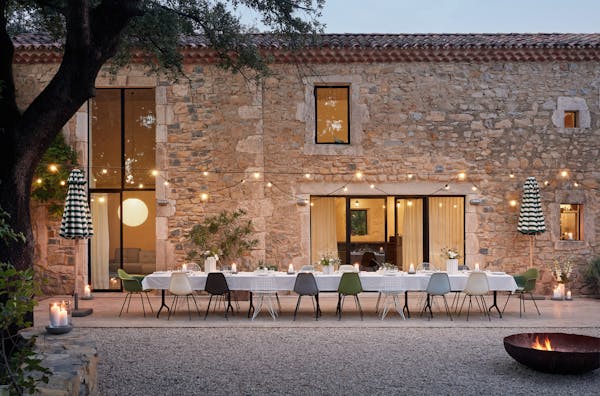 Courtyard with a long white-covered dining table and many different chairs at dusk