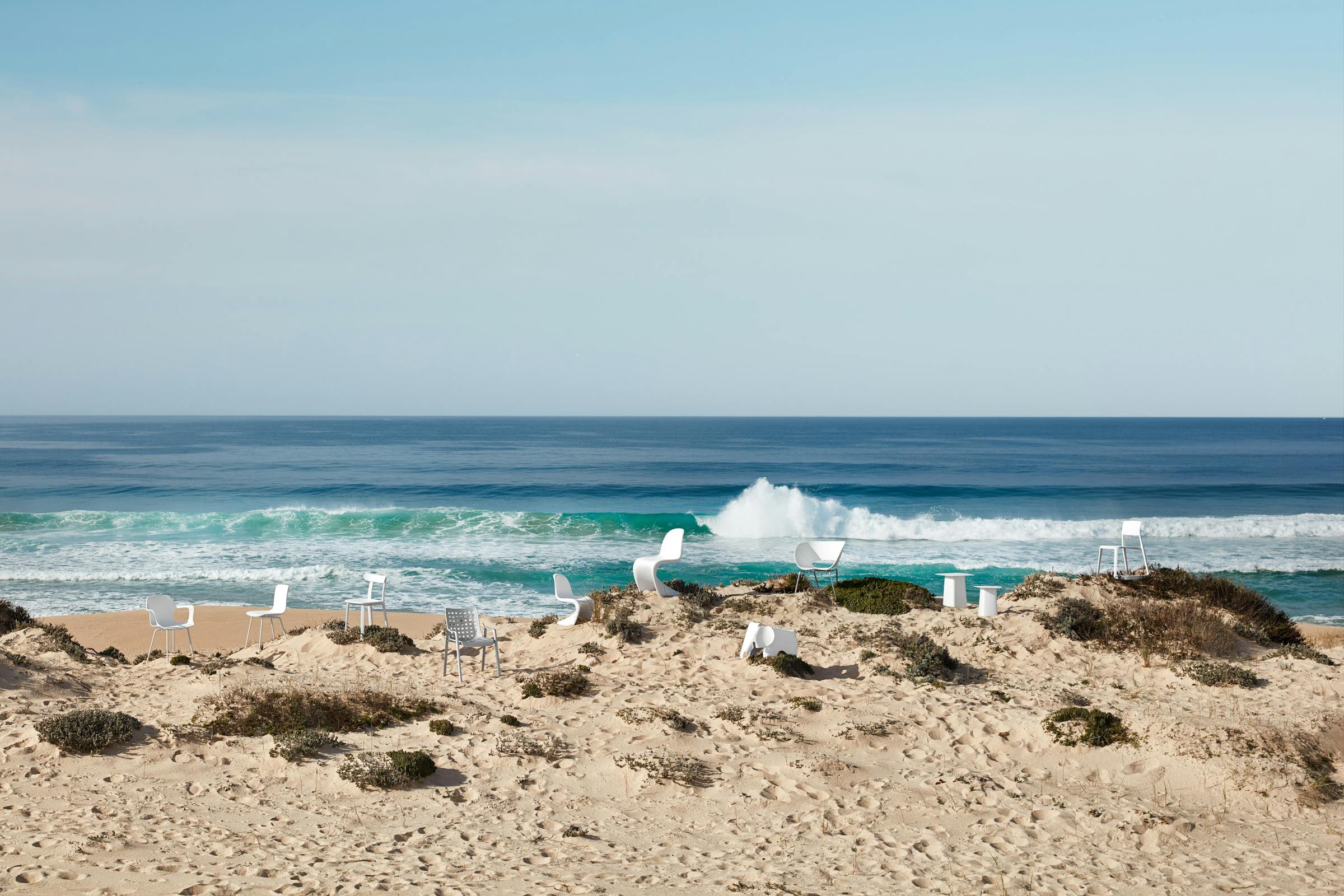 A large group of different white chairs in the dunes with the blue sea