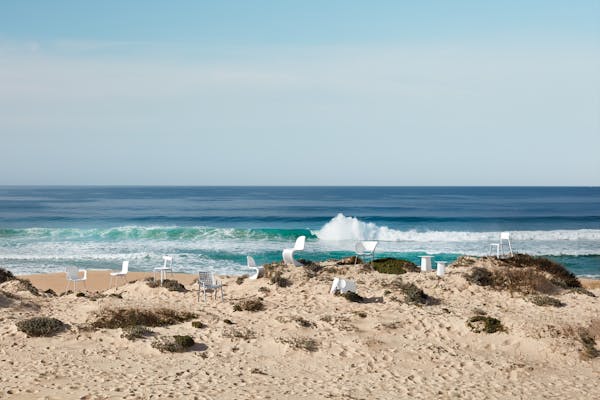 A large group of different white chairs in the dunes with the blue sea
