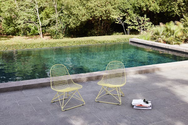 two low yellow Eames wire chairs by the turquoise pool in summer
