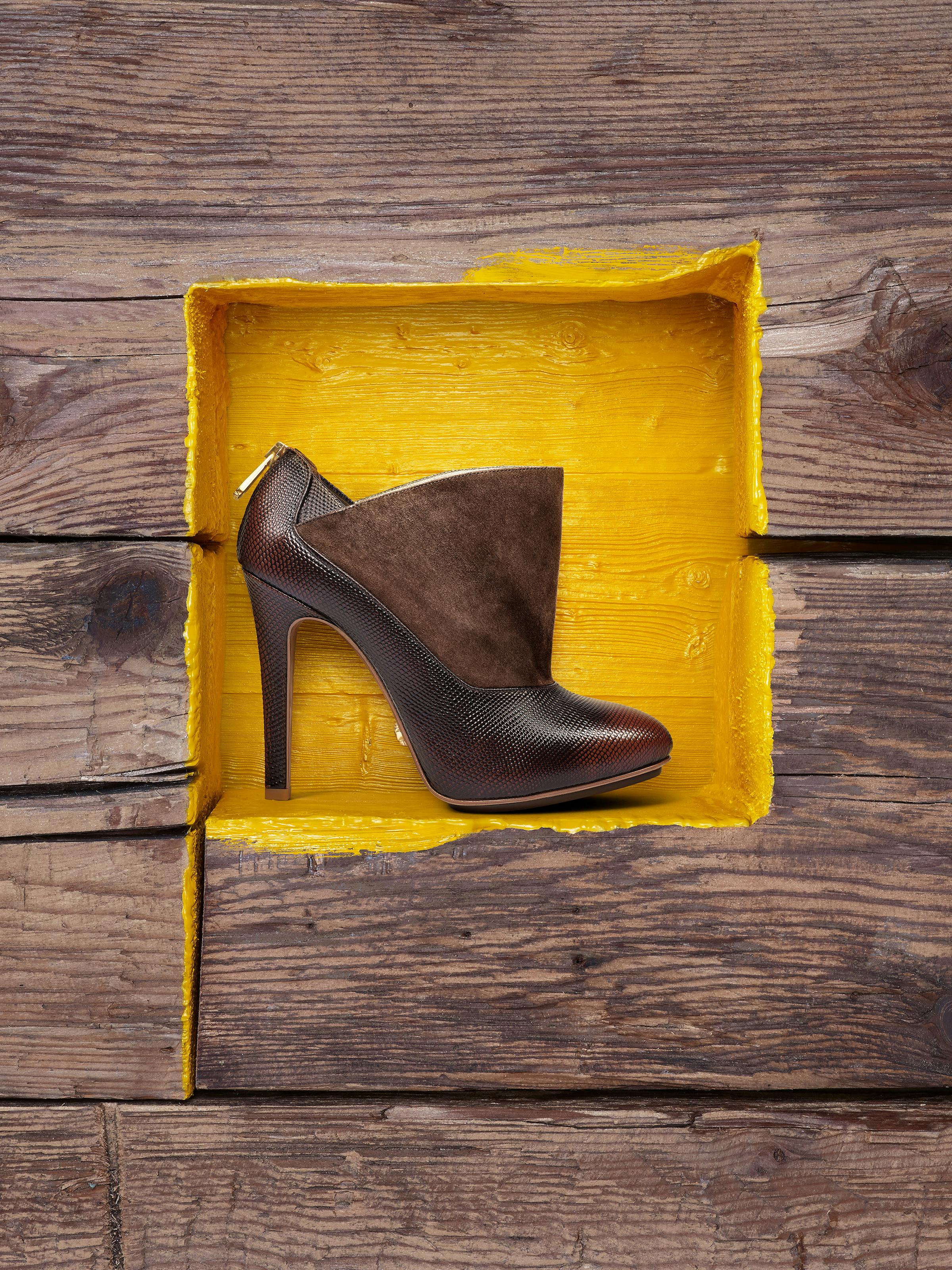 a dark brown high heel in front of a yellow painted wooden wall