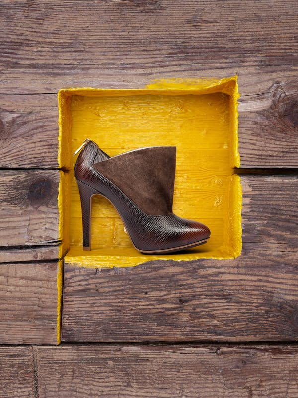 a dark brown high heel in front of a yellow painted wooden wall