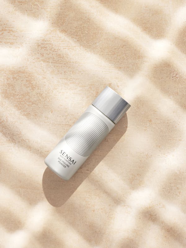 White cosmetic product on beige travertine with sun streaks.