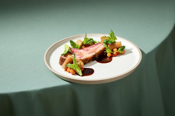 Plate with sous-vide cooked veal cutlet arranged with vegetables on a green table cloth