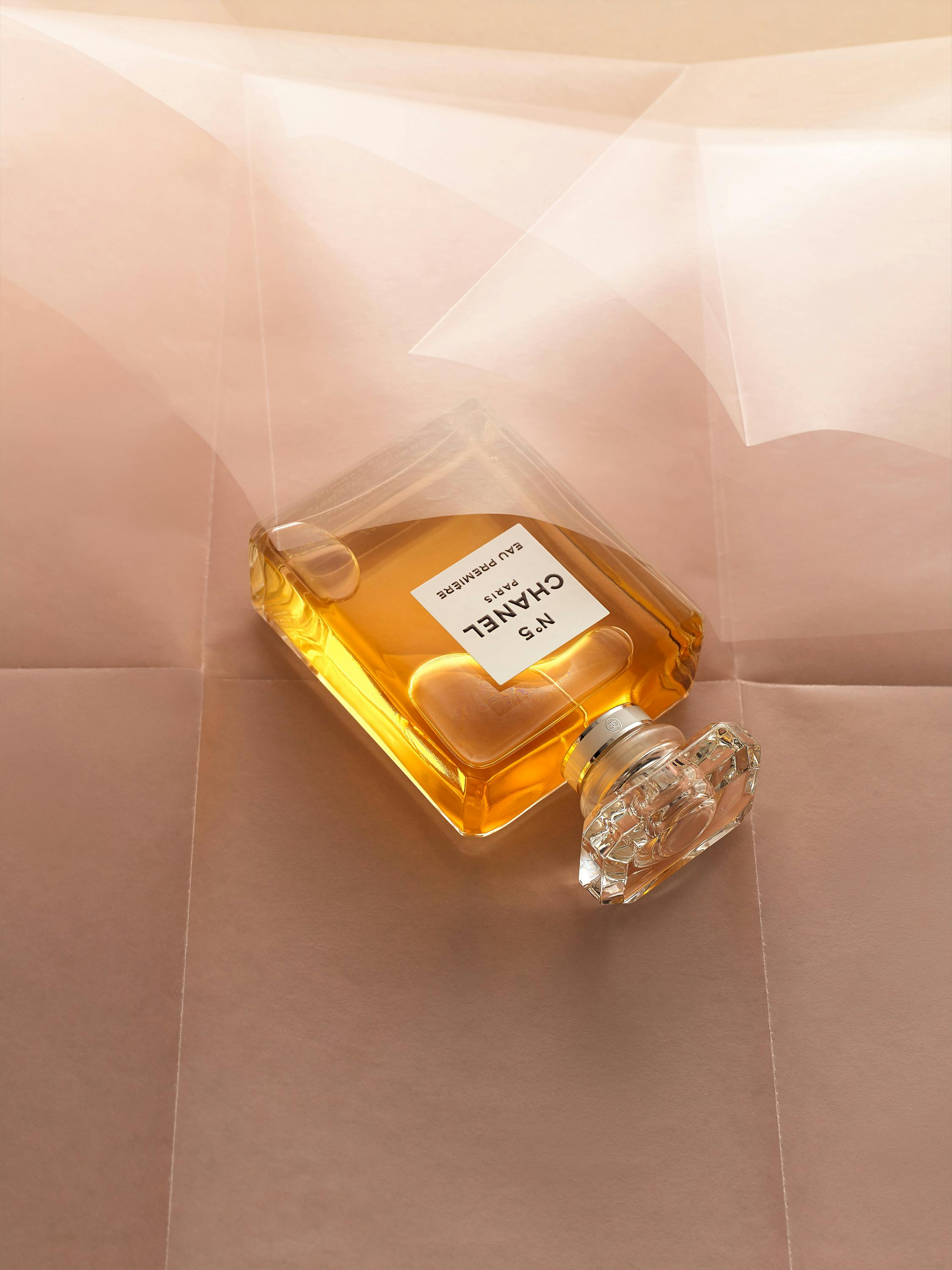 A Chanel perfume sits on a wavy pink paper.