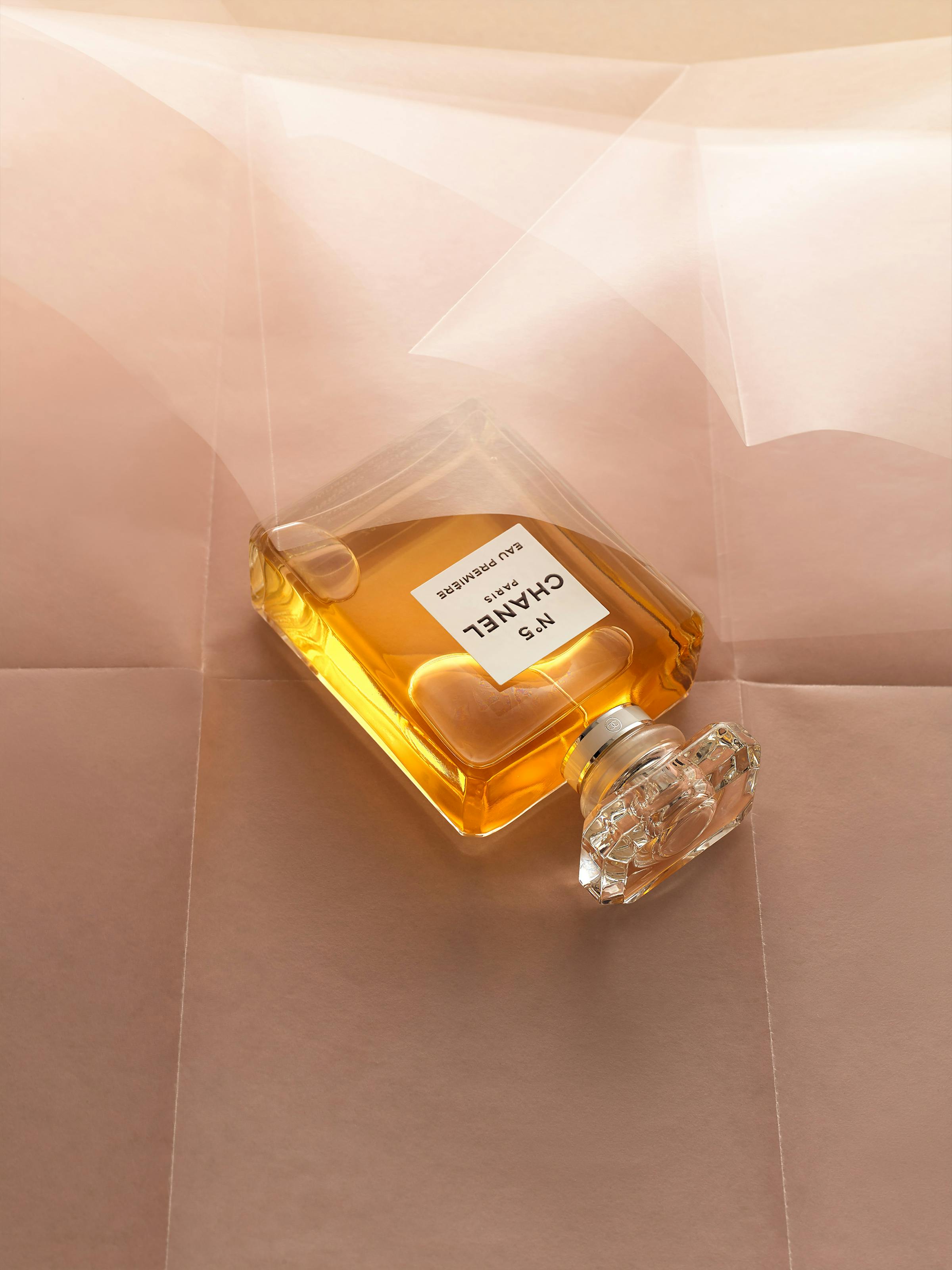 A Chanel perfume sits on a wavy pink paper.