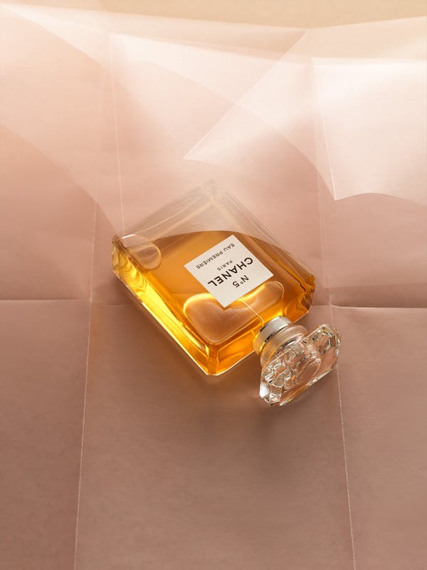 A Chanel perfume sits on a wavy pink paper.