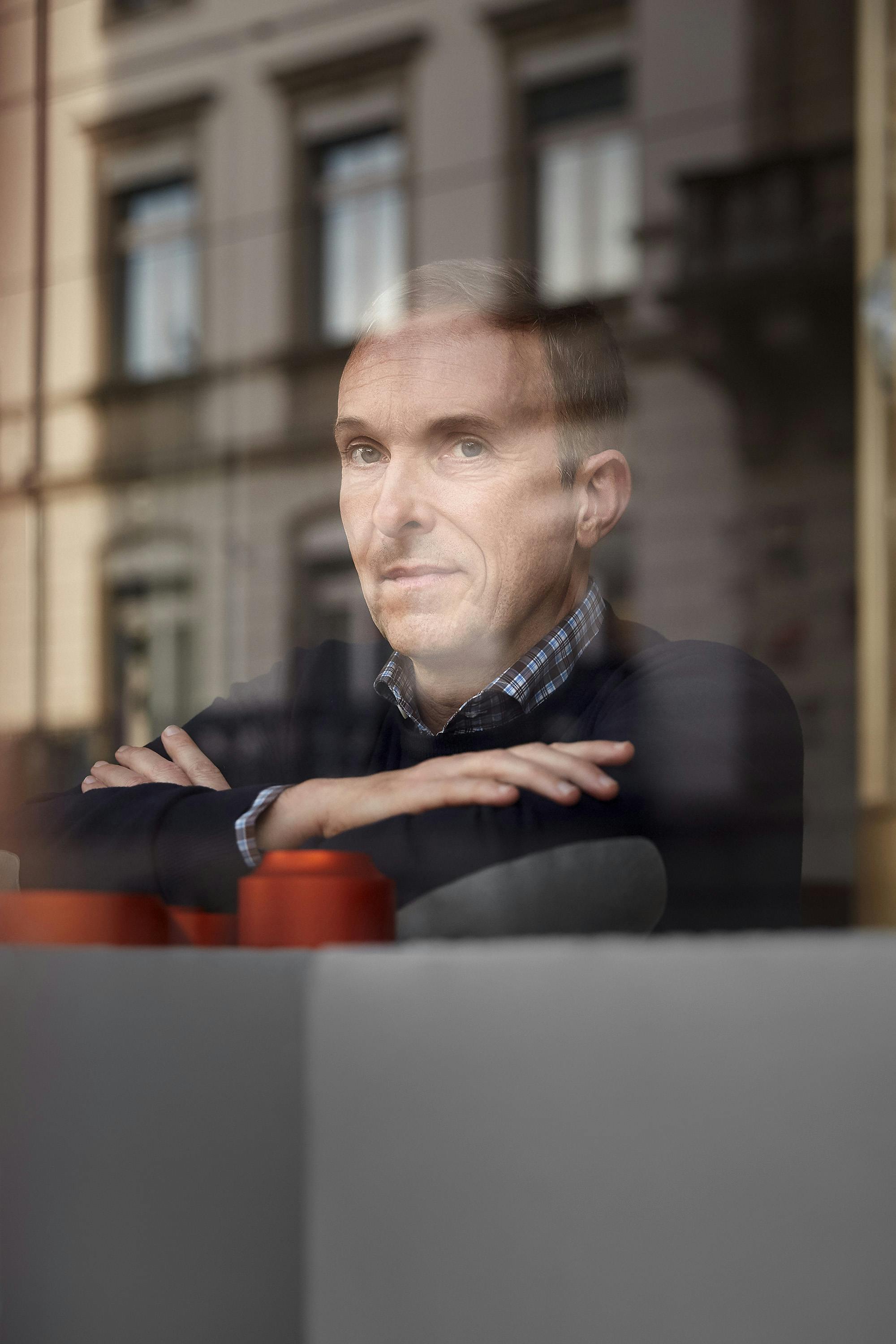 Portrait of designer Frédéric Dedelley looking out of a window, with reflections of a classical building