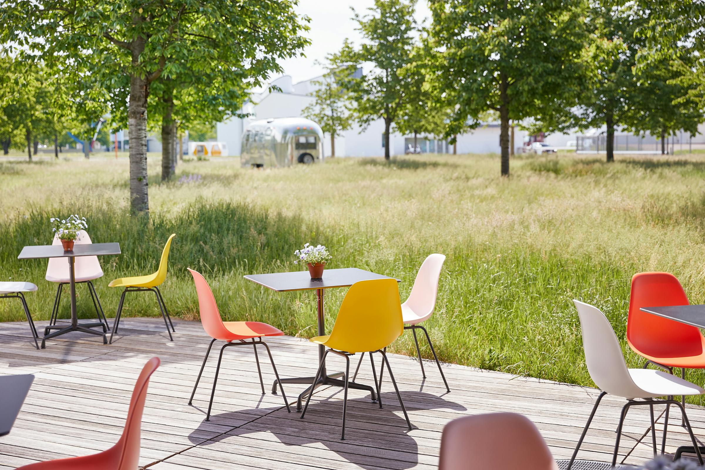 Terrace with outdoor tables and Eames chairs in front of a lush green lawn