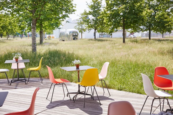 Terrace with outdoor tables and Eames chairs in front of a lush green lawn