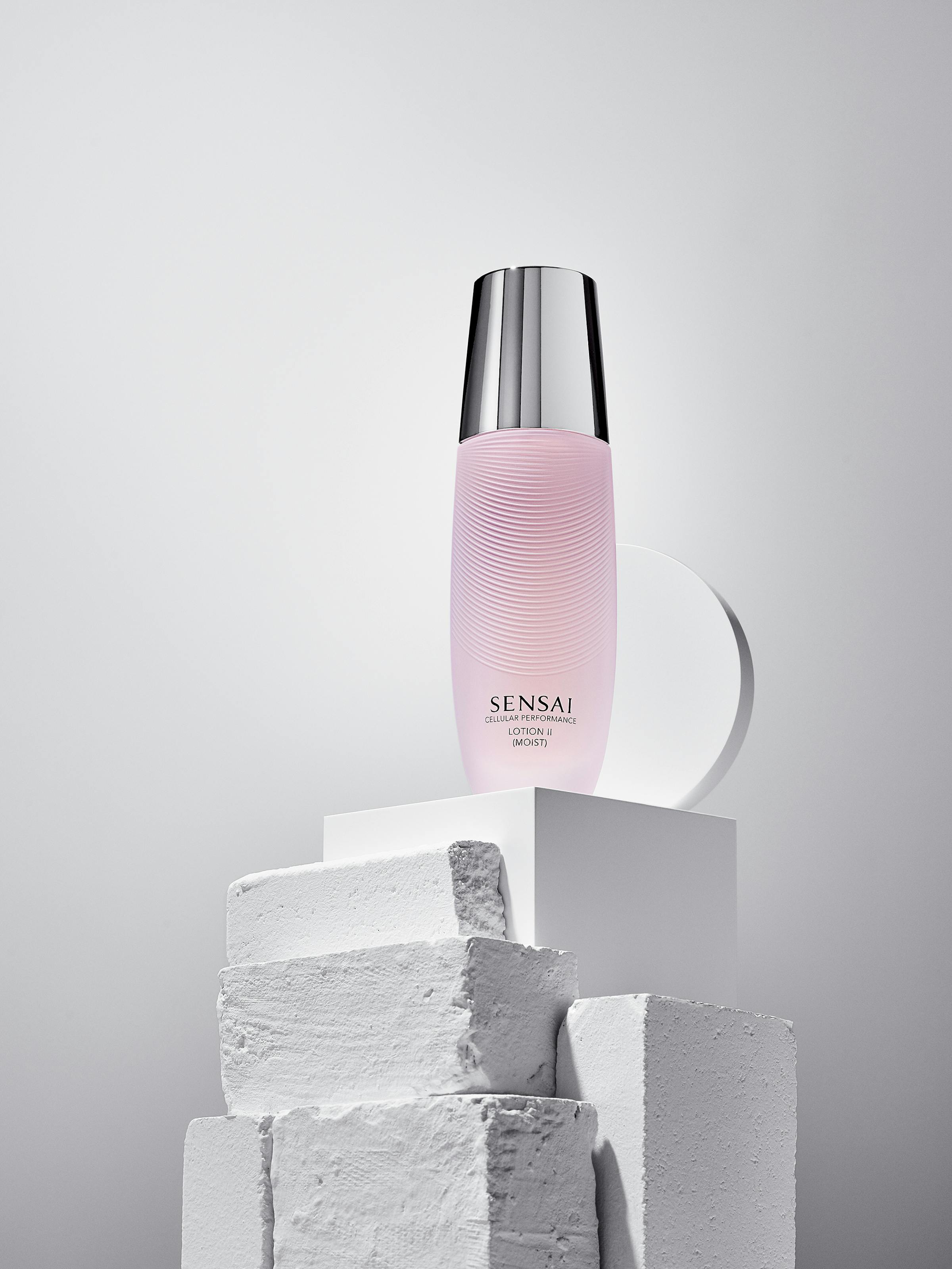 Pink lotion in a glass bottle on white painted stones