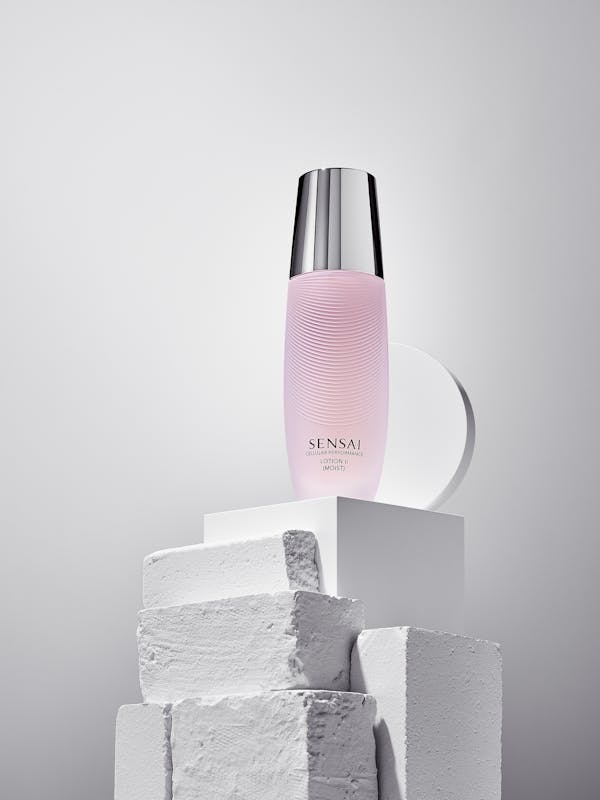 Pink lotion in a glass bottle on white painted stones