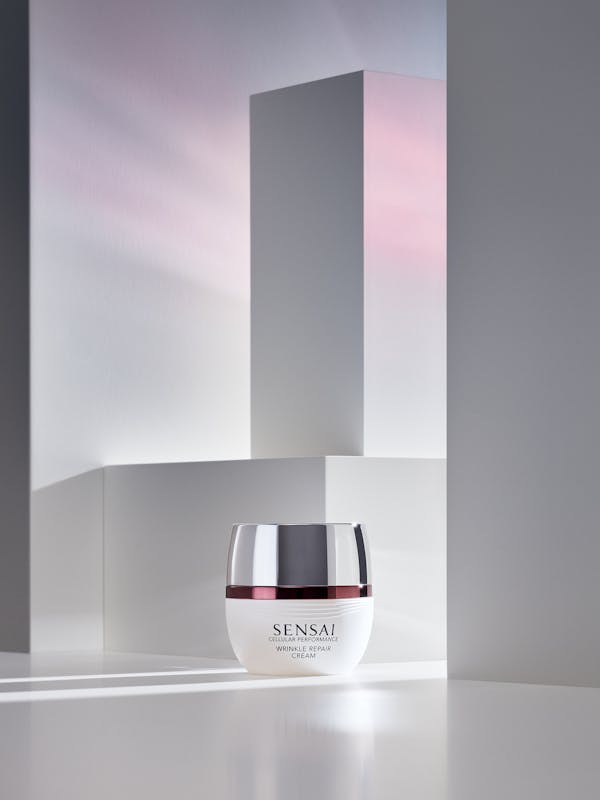A white box containing beauty cream i a set of white pedestals, with red light shining in from the right-hand side.