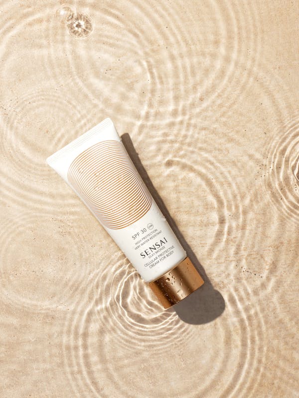 White sun cream tube with golden cap in a water basin with travertine base 