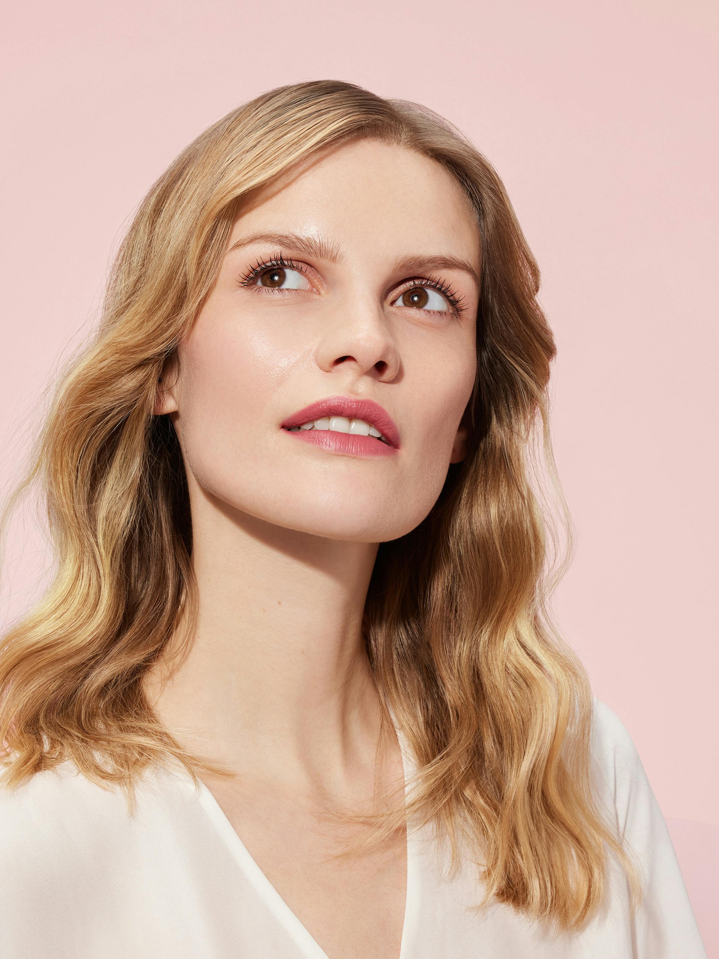 Beauty shot of a blonde woman in front of a light pink background