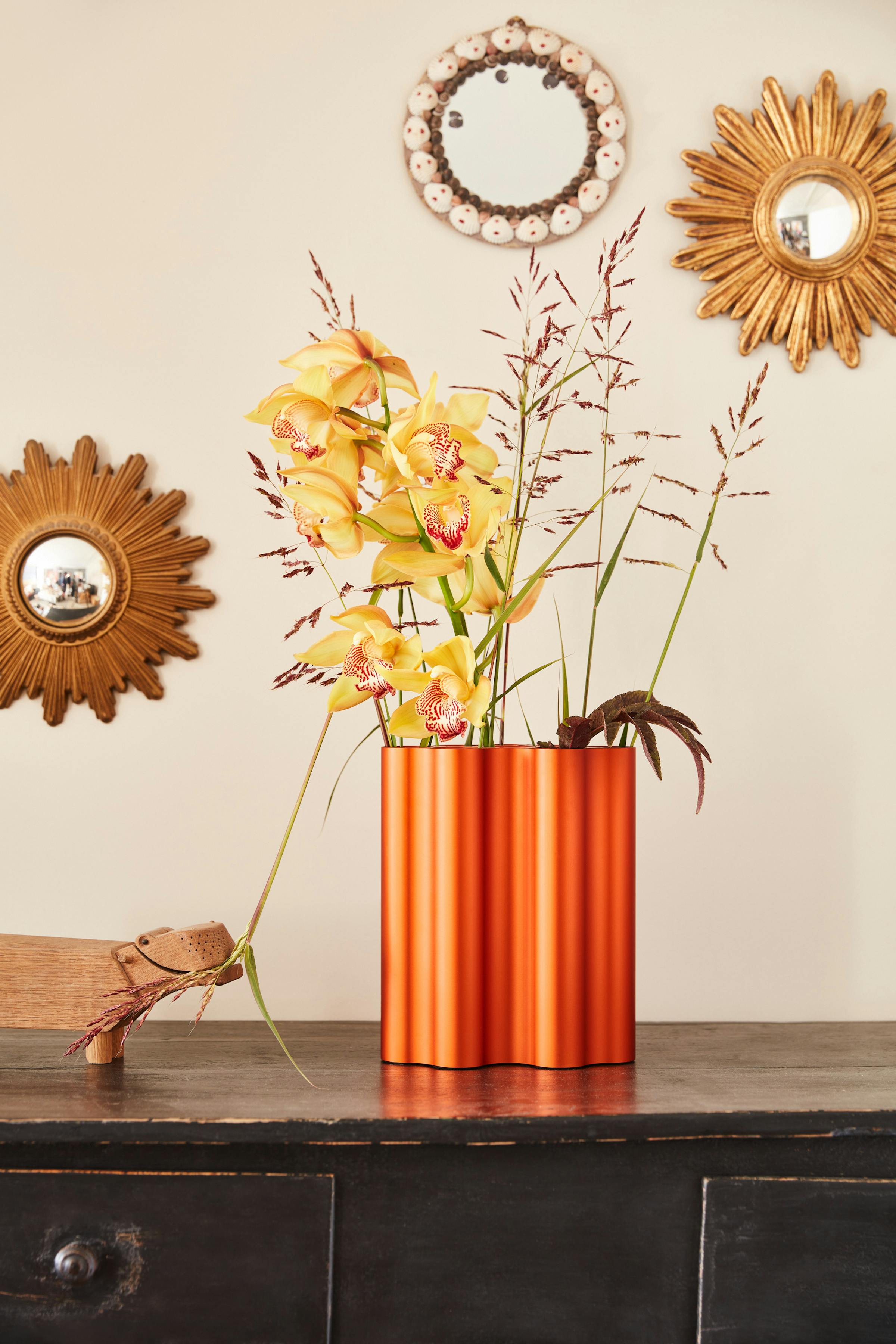 An orange Nuage vase by the Bouroullec brothers with flowers, from which a wooden toy hippopotamus is pulling.