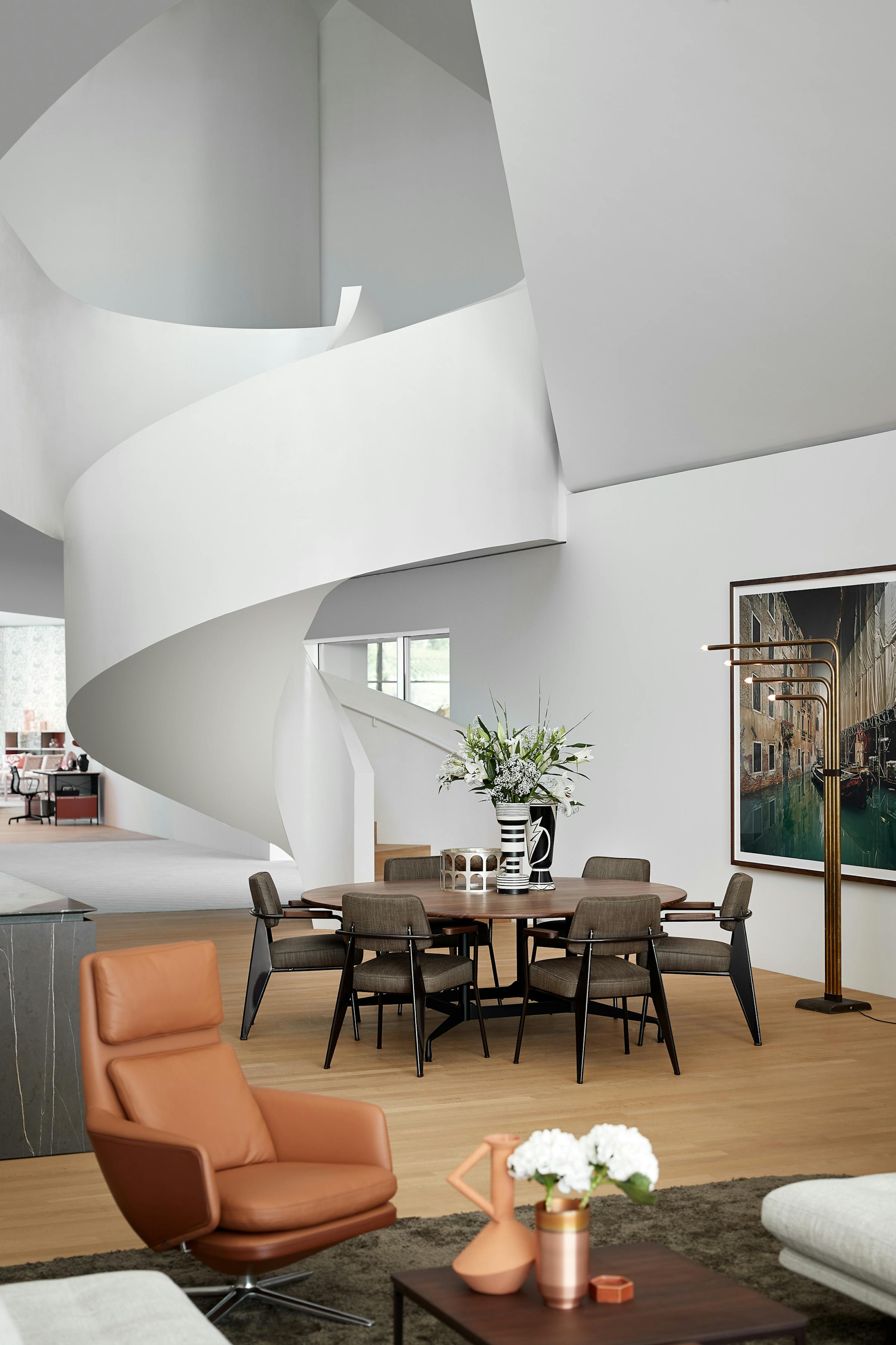 Round dining table made of dark wood in front of a sculpturally curved white staircase