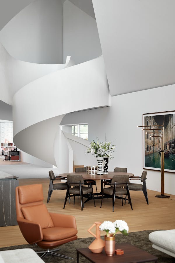 Round dining table made of dark wood in front of a sculpturally curved white staircase