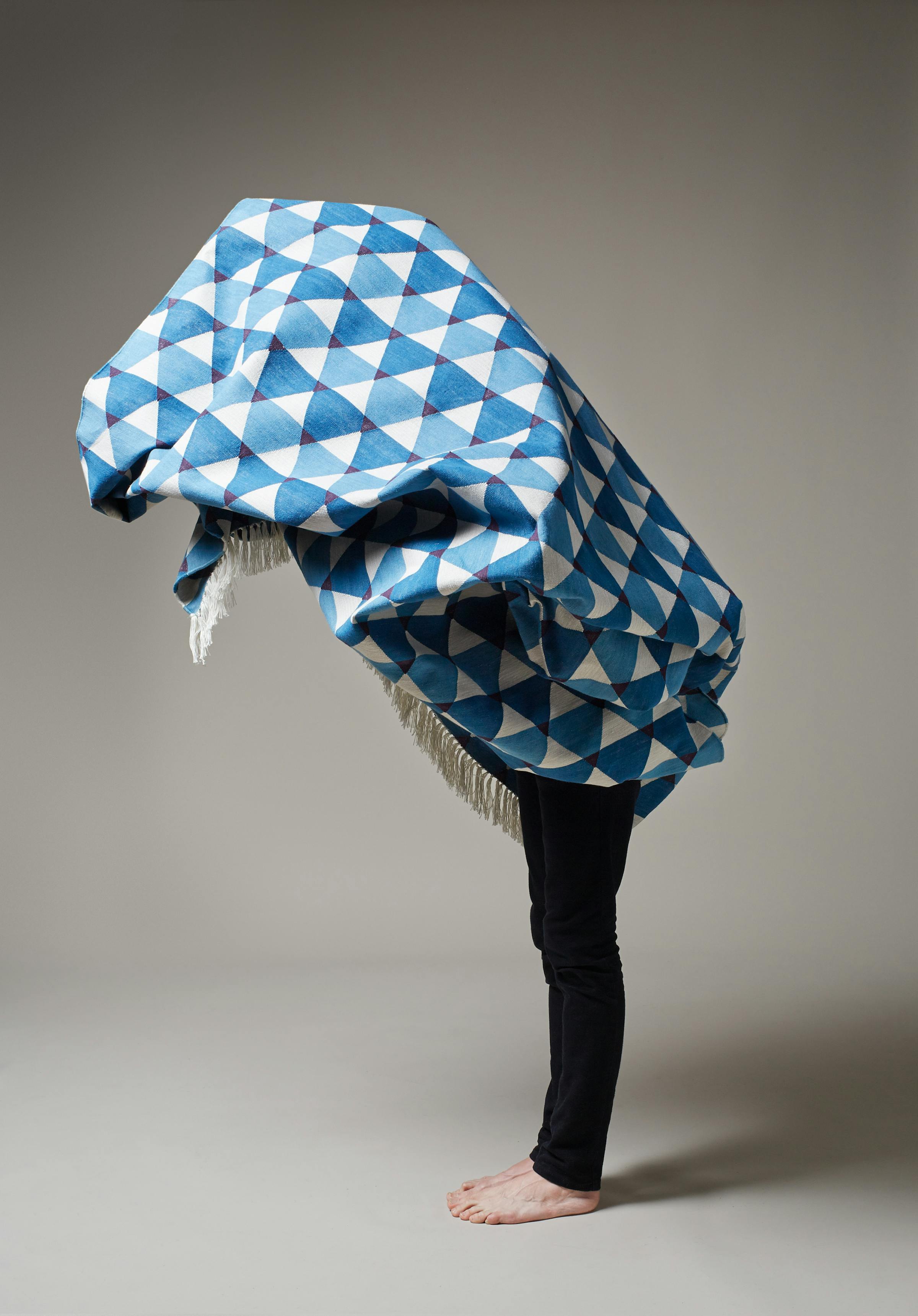 A man wearing black trousers is carrying a blue and white carpet and looks like a ostrich.