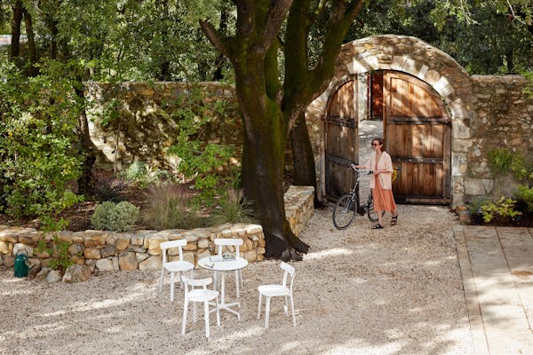 White outdoor table with four white chairs on a gravel area and a young woman with a bicycle