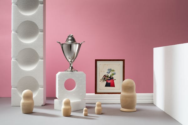 Classic silver object and a painting of two men kissing surrounded by wooden babushkas in a set design of whiite styrofoam objects