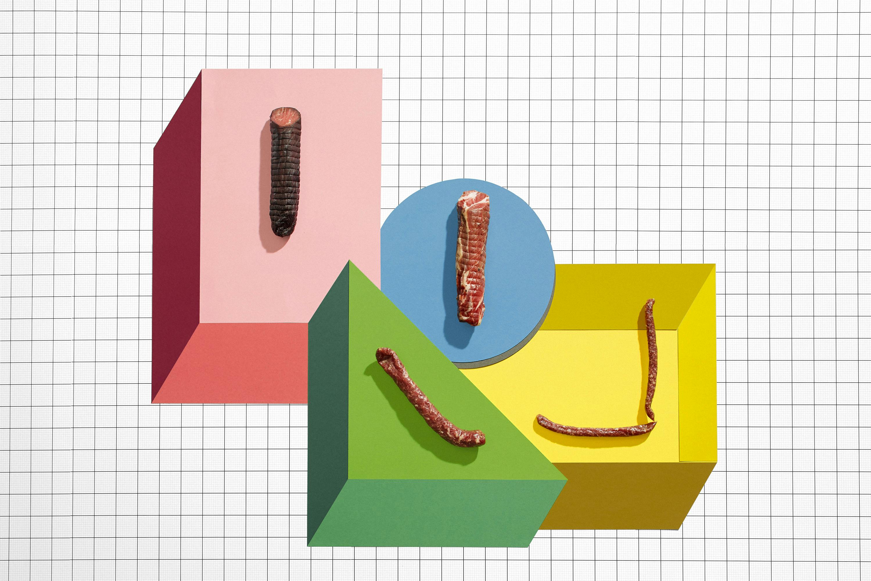A group of 4 dry sausages in an abstract graphic set made of colourful paper in the shapes of a circle, square and triangle.