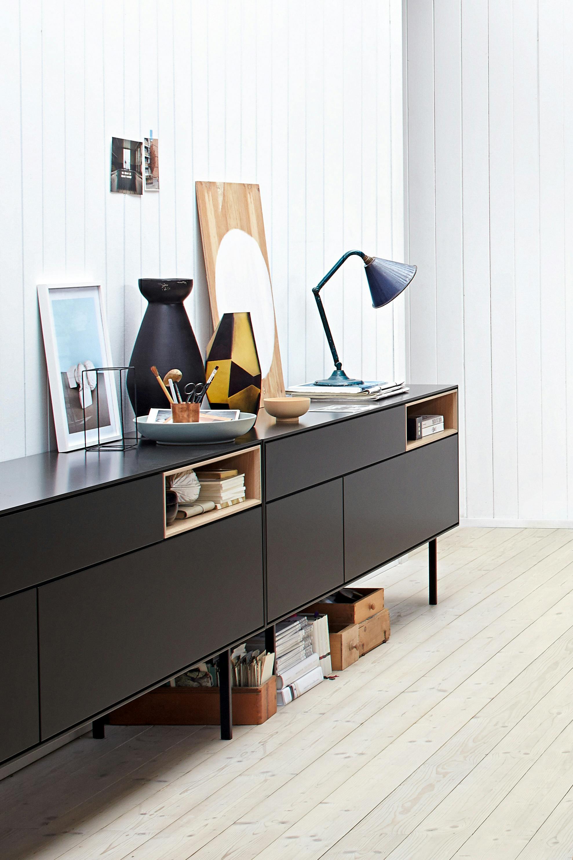 Close-up of a long black sideboard with pictures and a table lamp