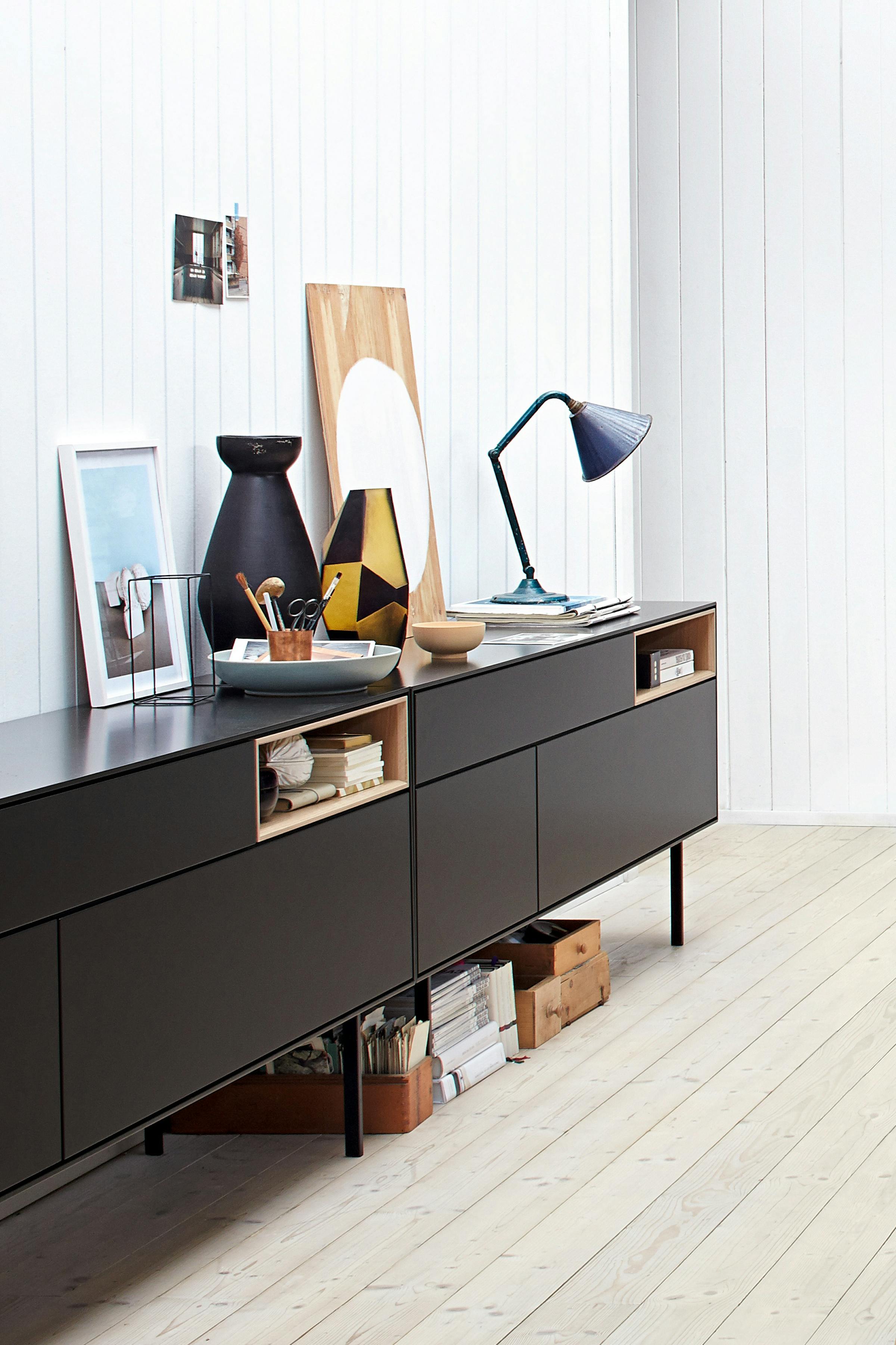Close-up of a long black sideboard with pictures and a table lamp