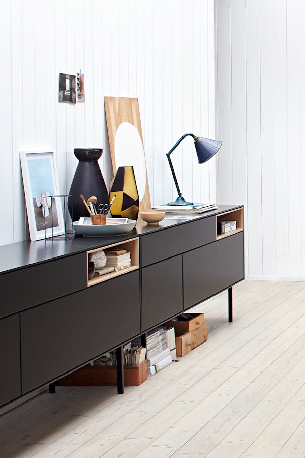 Close-up of a long black sideboard with pictures and a table lamp