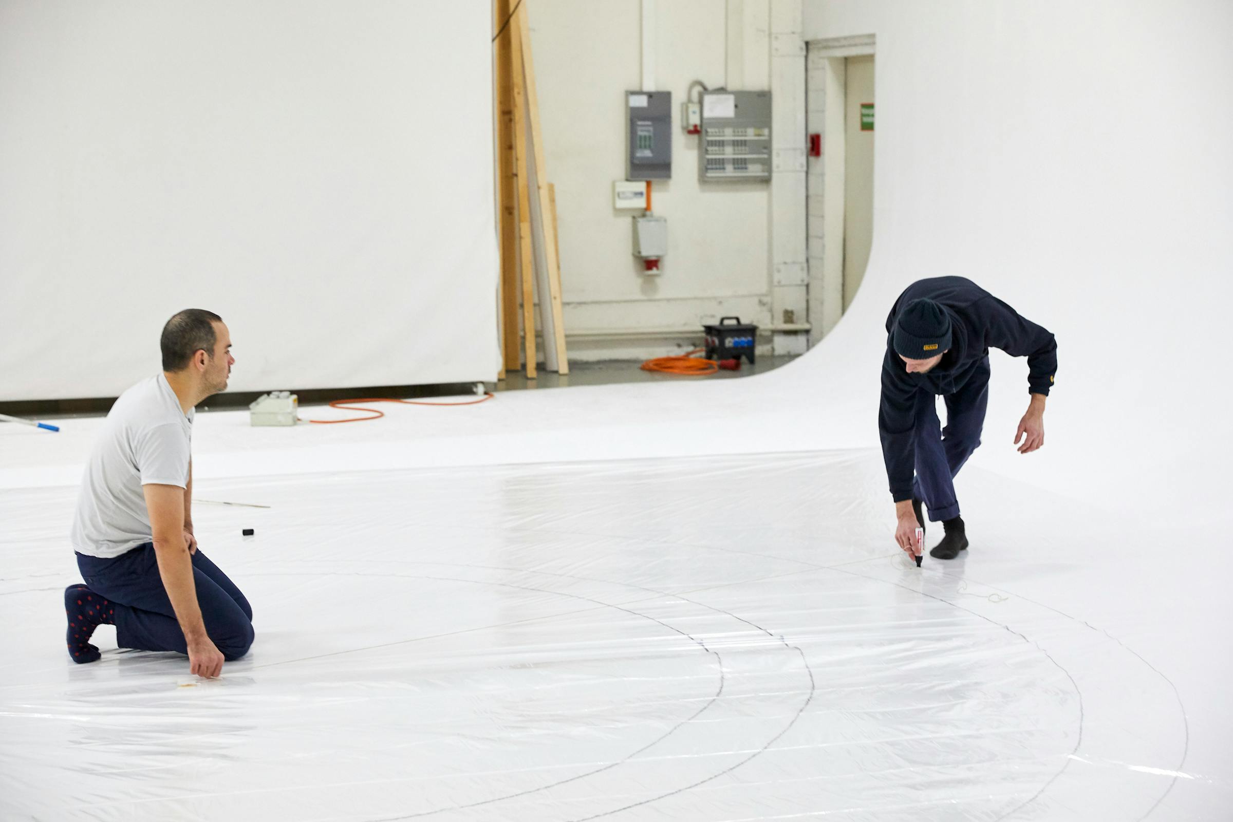Lorenz Cugini and an assistant draw lines on a white floor.