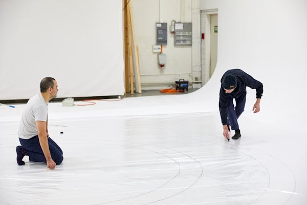 Lorenz Cugini and an assistant draw lines on a white floor.