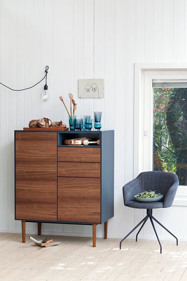 A wooden highboard with a blue side panel and an armchair on the side.