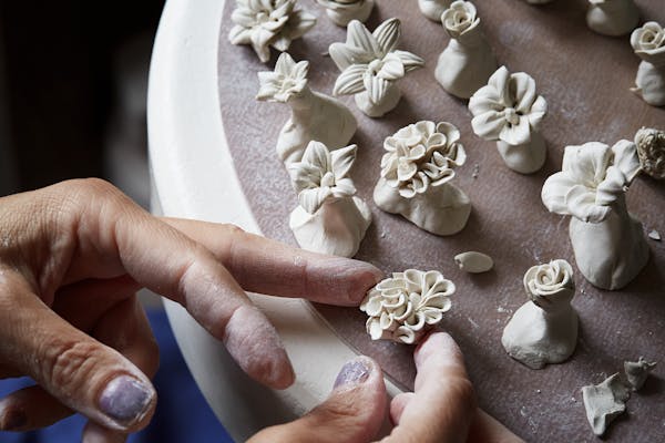 Hand of a ceramist shaping small white porcelain flowers