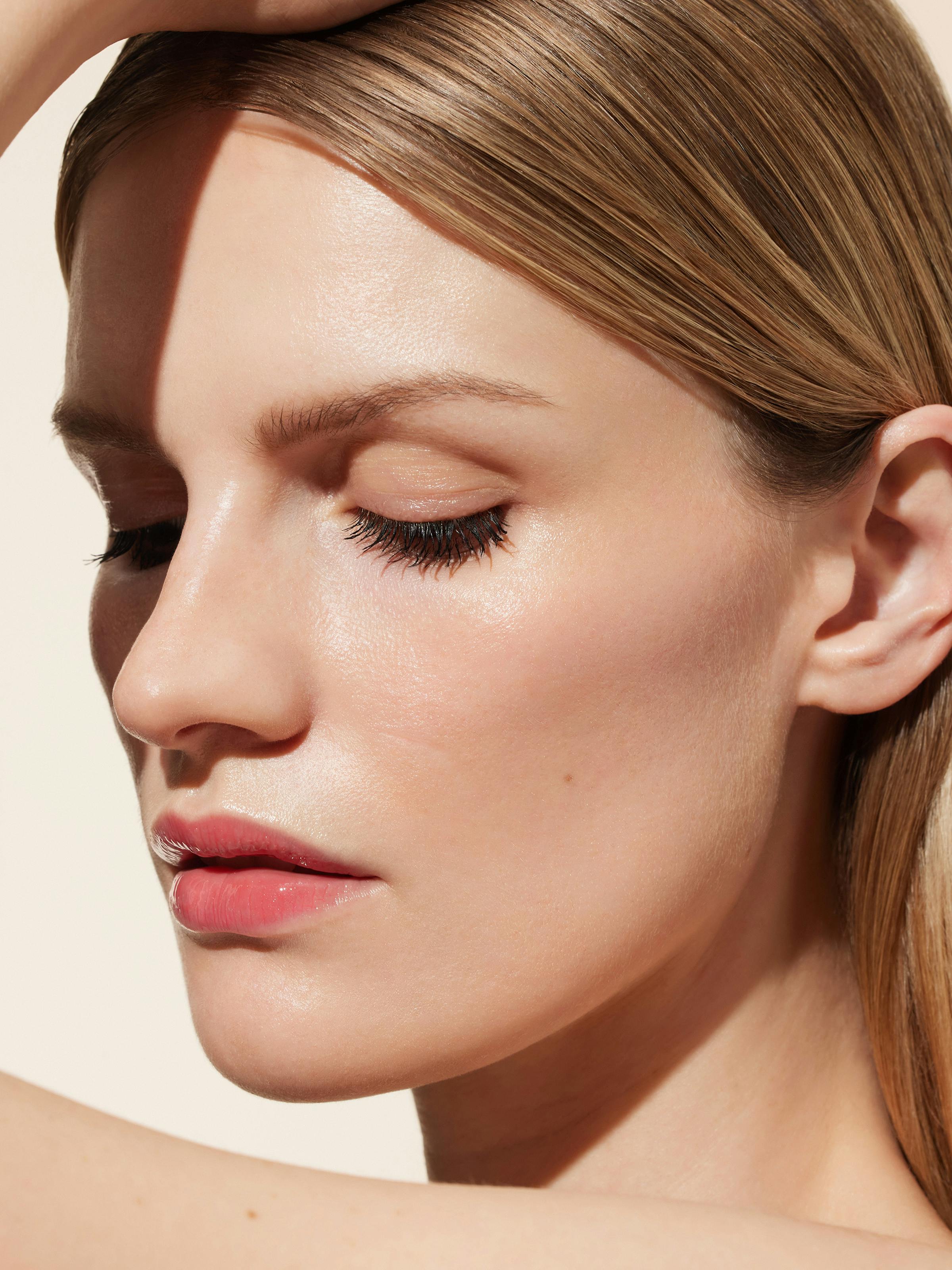 Beauty shot of a blonde woman in front of a light beige background and sunny light