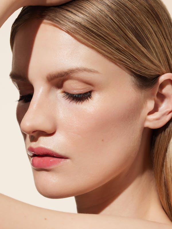 Beauty shot of a blonde woman in front of a light beige background and sunny light