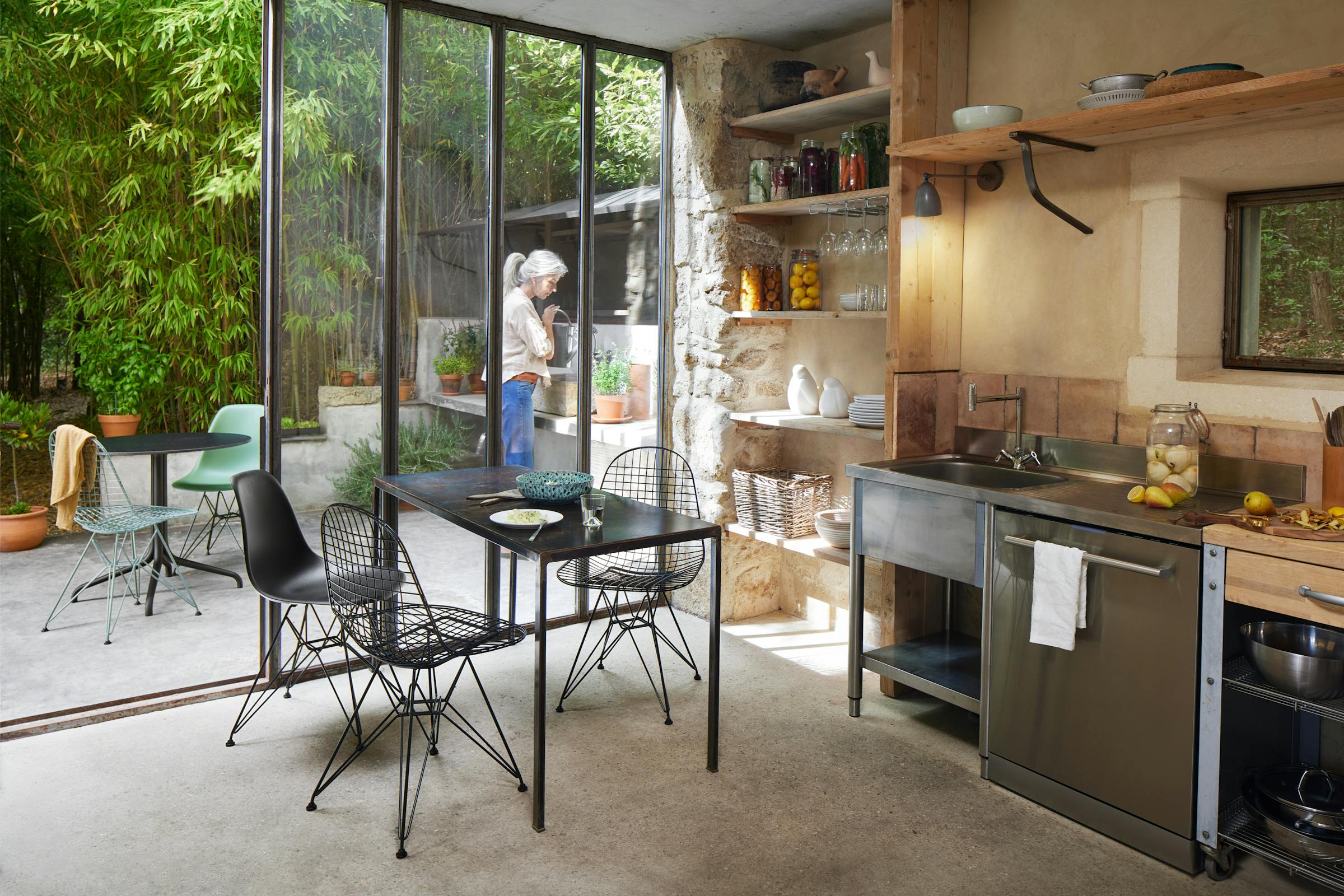 Small kitchen with three black Eames chairs, woman gardening in the back yard